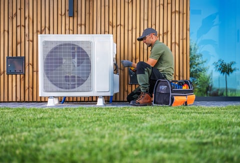 Technician servicing air conditioning unit beside a modern home